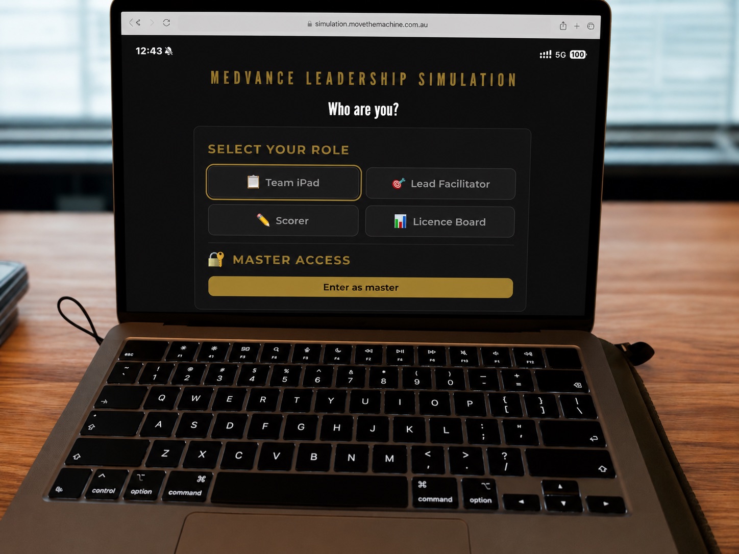 A laptop showing the simulation platform role selection screen with facilitator, scorer and licence board access